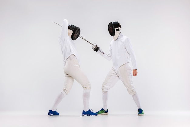 Free photo the two men wearing fencing suit practicing with sword against gray