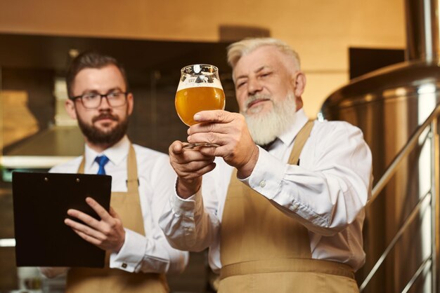 Due uomini che indossano mantenendo un bicchiere di birra ed esaminando la qualità