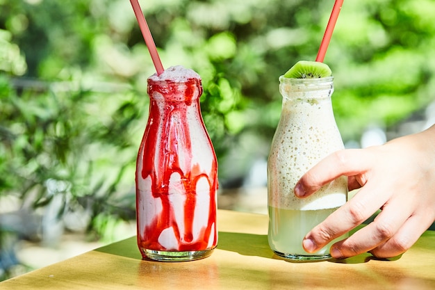 Two milkshakes grabbed by a hand on wooden table