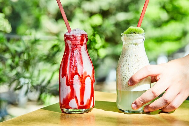 Two milkshakes grabbed by a hand on wooden table