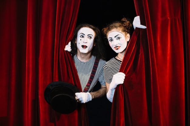 Two mime artist peeking through red curtain