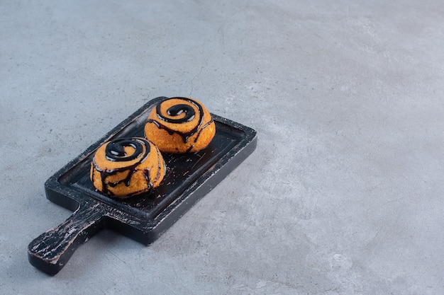 Two mini cakes decorated with chocolate glaze on black board.