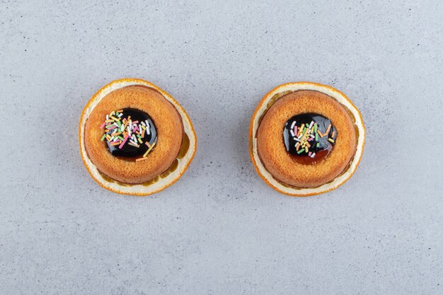 Two mini cakes with jelly placed on top of slice of orange. High quality photo