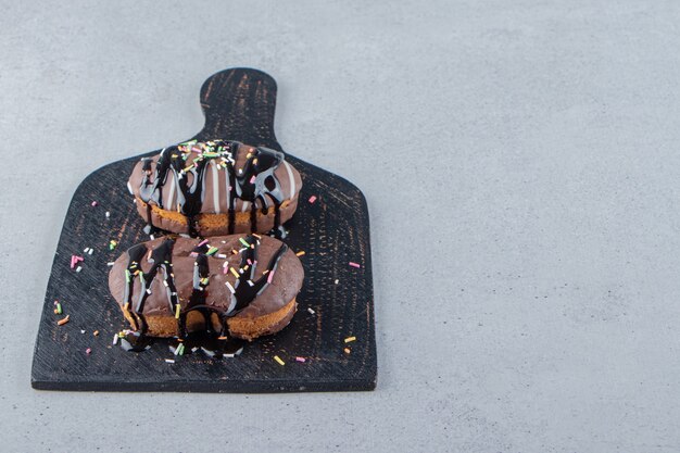 Two mini chocolate cakes with sprinkles on black cutting board