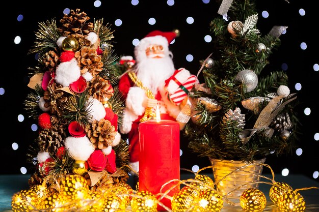 Two mini christmas trees and a santa claus figurine on black background with bokeh lights on it