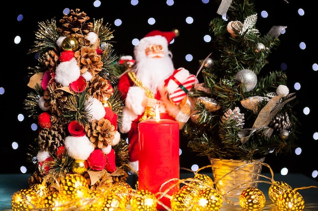 Two mini christmas trees and a santa claus figurine on black background with bokeh lights on it