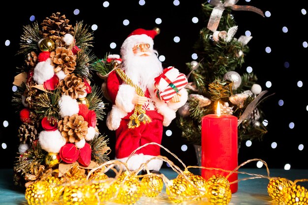 Two mini christmas trees and a santa claus figurine on black background with bokeh lights on it