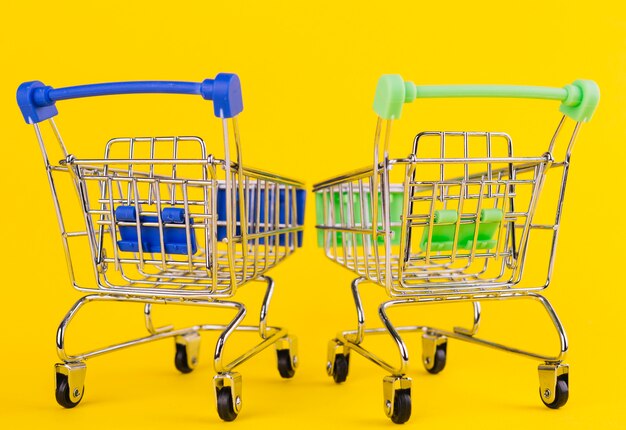 Two miniature green and blue shopping cart on yellow background