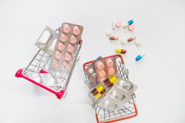 Two miniature shopping carts filled with pills blister on white background