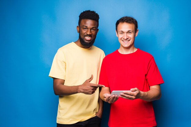 Two mixed race men looking at the phone isolated on blue wall