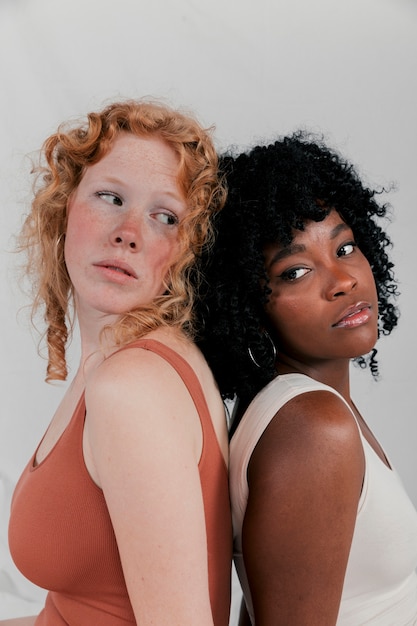 Two multi ethnic female friends standing back to back against grey backdrop