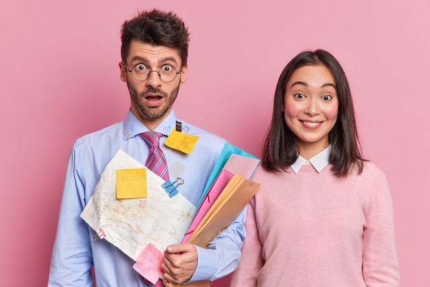 Two multiethnic woman and man colleagues meet in office for creating presentation carry documents and stickers with information prepare for workshop or have courses together. Young classmates