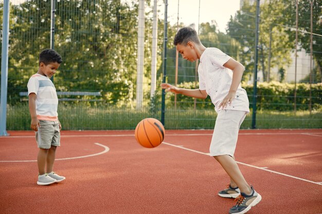 Two multiracional brothers playing basketball on a court near the park