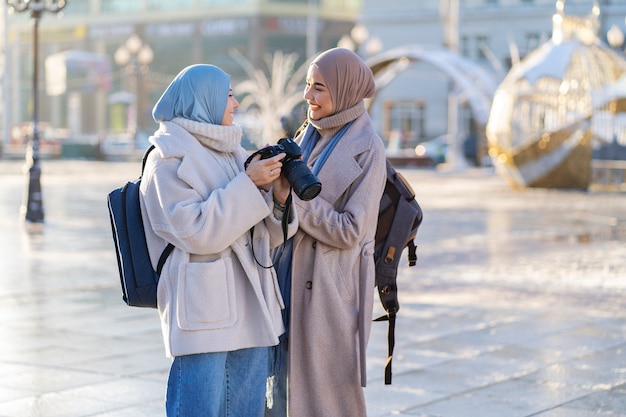 街を歩き、旅行中に写真を撮る2人のイスラム教徒の女性の友人