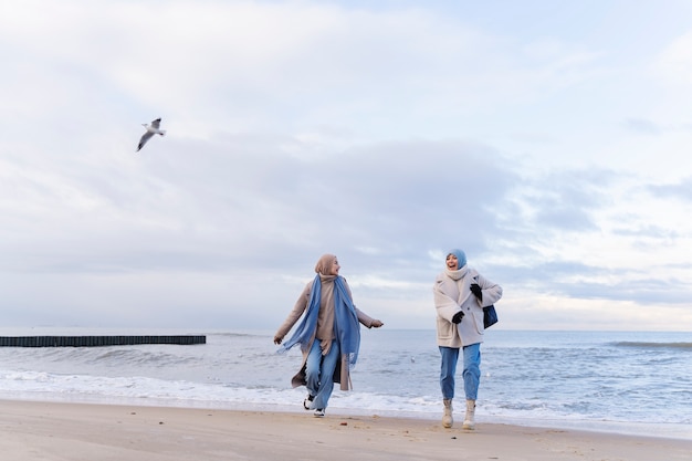 Бесплатное фото Две подруги-мусульманки гуляют по пляжу во время путешествия