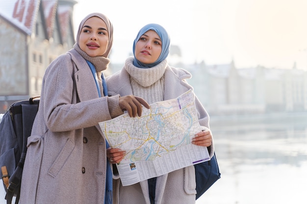 Two muslim women with hijabs consulting a map while traveling in the city