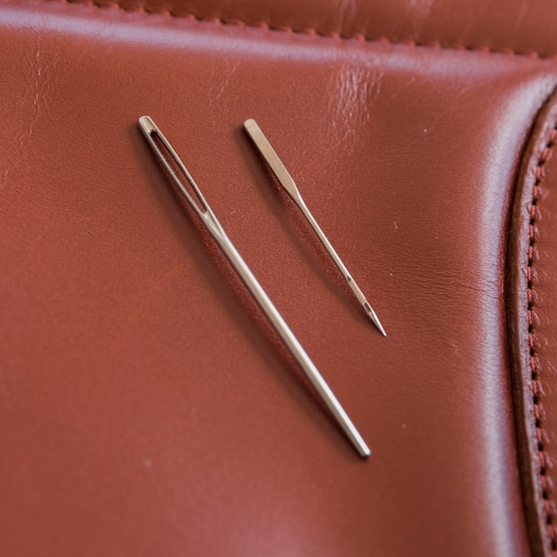 Two needles on brown leather with handmade stitches