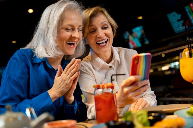 Две подруги старшего возраста пользуются смартфоном в ресторане