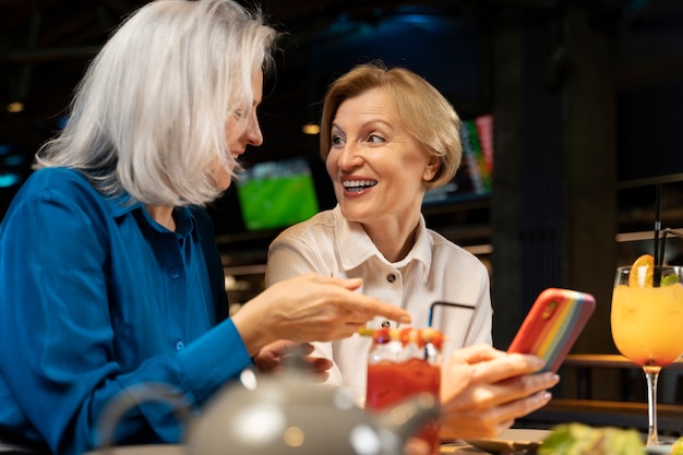 Two older female friends using a smartphone at a restaurant