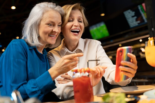 레스토랑에서 스마트폰을 사용하는 두 나이 많은 여자 친구