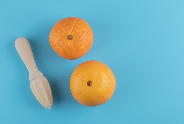Two oranges and wooden reamer on blue table. 