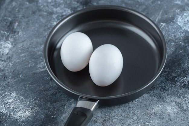 Due uova di gallina organiche in padella nera.