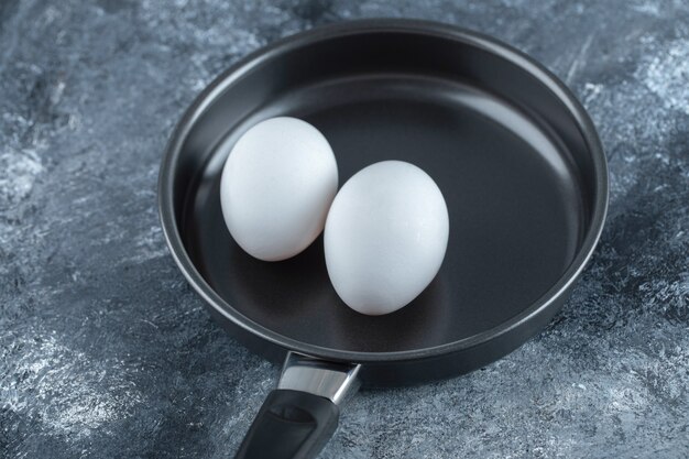 Два органических куриных яйца на черной сковороде.