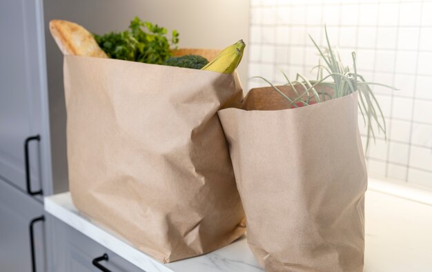 新鮮な農産物が入ったキッチンカウンターの2つの紙の買い物袋