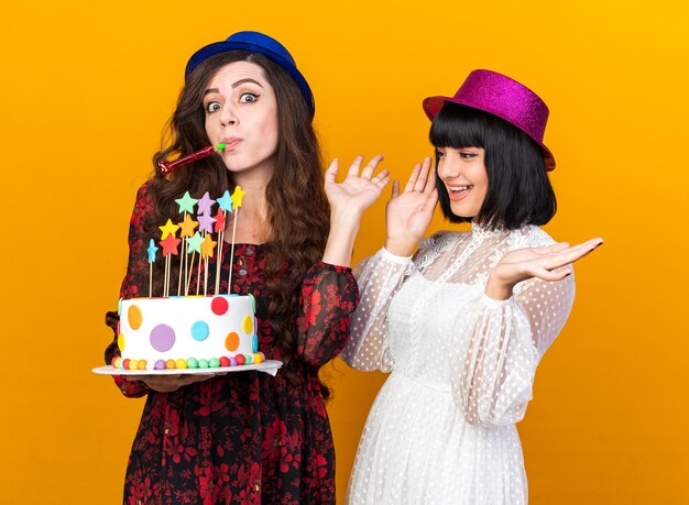 Two party women wearing party hats and holding cake with stars