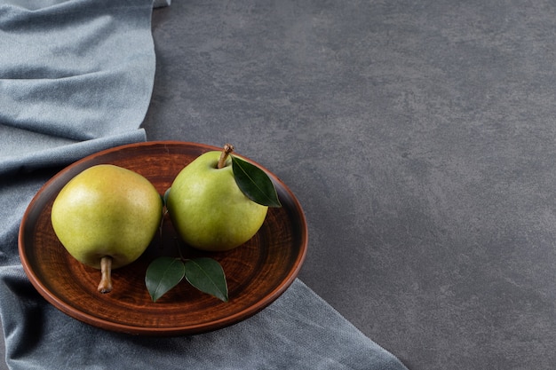 Free photo two pears on a wooden plate on a pieces of fabric on the marble surface