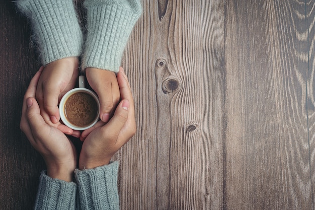 Two people holding cup of coffee in hands with love and warmth on wooden table