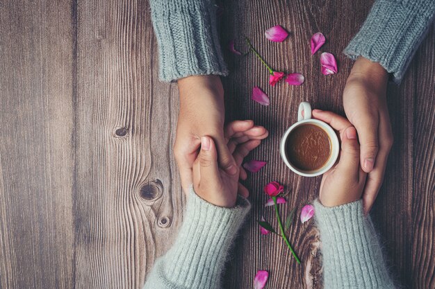 Two people holding cup of coffee in hands with love and warmth on wooden table