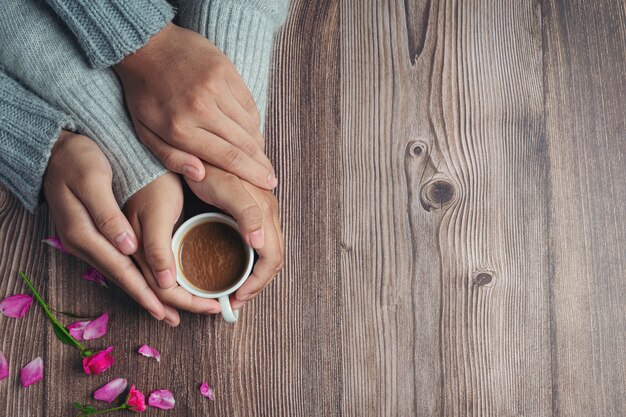 Two people holding cup of coffee in hands with love and warmth on wooden table