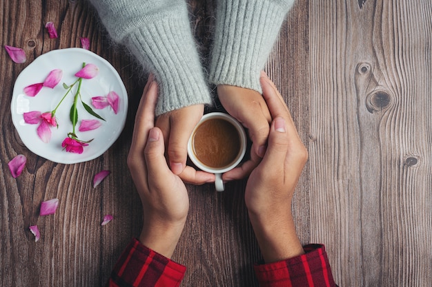 Two people holding cup of coffee in hands with love and warmth on wooden table