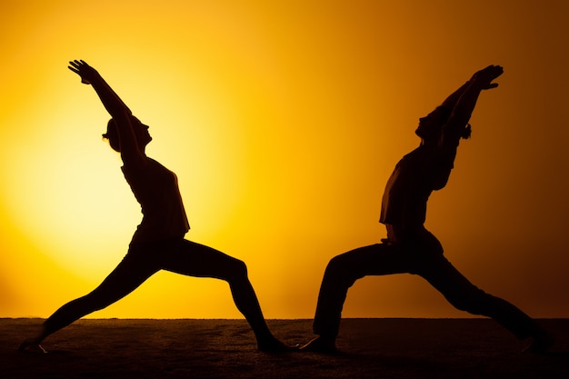 Free photo two people practicing yoga in the sunset light