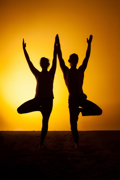 Foto gratuita due persone che praticano yoga nella luce del tramonto