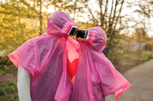 Два человека романтически смотрят друг на друга в розовых пластиковых плащах и VR-шлеме