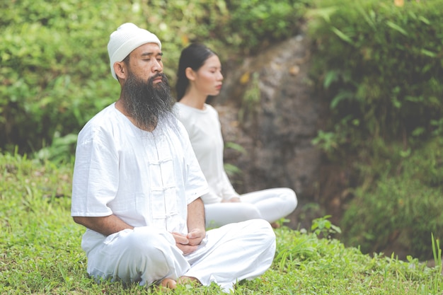 Two people in white outfit meditating in nature