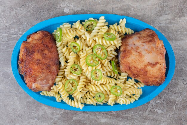 Two pieces of meat and peppered fusilli pasta on the wooden tray , on the marble.