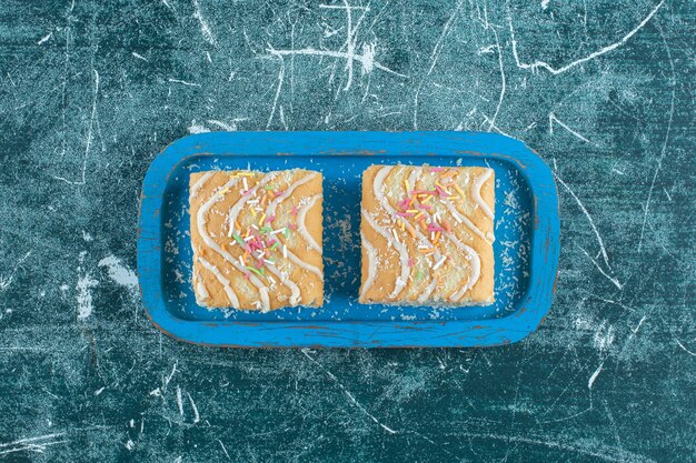 Два куска булочки на деревянной тарелке, на синем фоне. Фото высокого качества