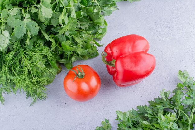 Two piles of various greens with tomato and pepper in between on marble background. High quality photo