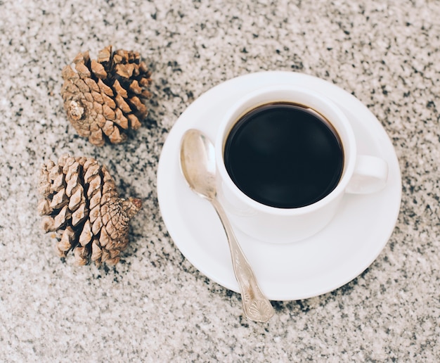 Two pinecones and cup of coffee on textured backdrop