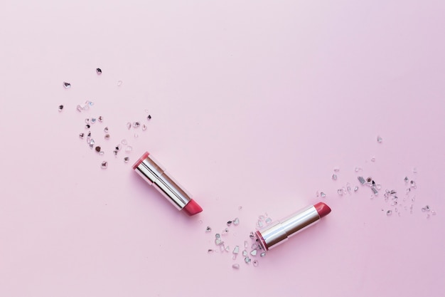 Two pink lipsticks with crushed glass pieces on pink background