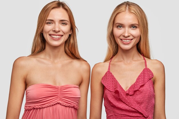 Two positive light haired young women in fashionable dresses, being in good mood