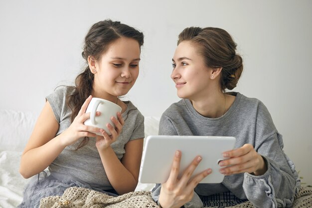 전자 태블릿에서 고속 인터넷 연결을 사용하여 집에서 온라인 쇼핑을하는 두 명의 긍정적 인 자매.