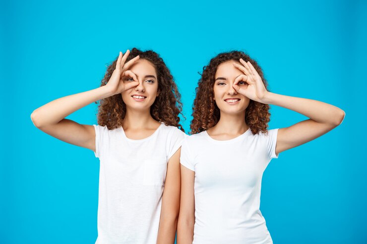 Free Photo two pretty girls twins smiling, joking over blue wall