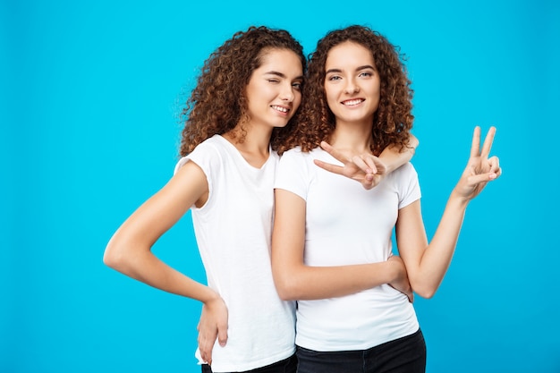 Foto gratuita due gemelli graziosi delle ragazze che sorridono, mostrando pace sopra la parete blu