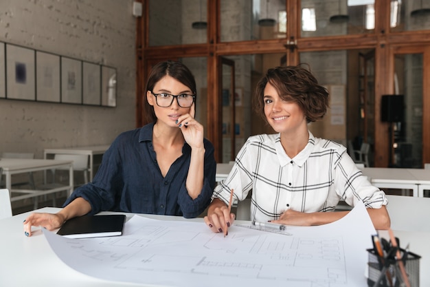 Two pretty smiling women sitting by the table