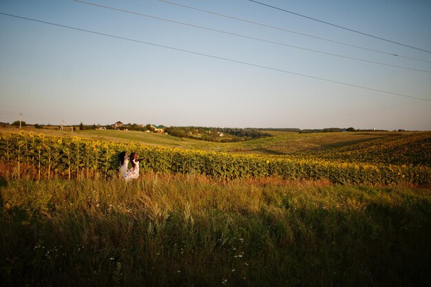 Two pretty young black friends woman wear summer dress pose in a sunflower field