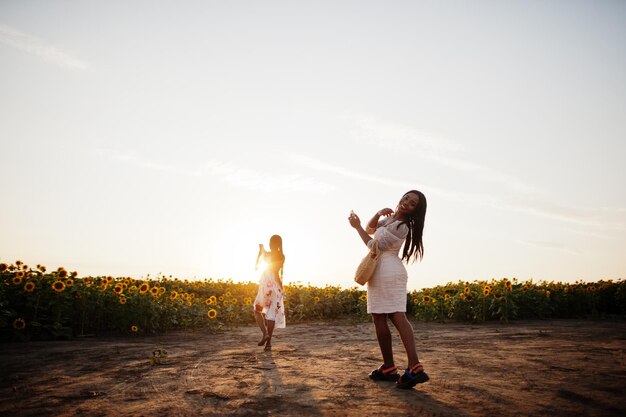 Two pretty young black friends woman wear summer dress pose in a sunflower field